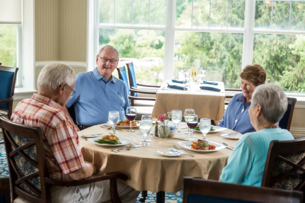 Four residents dine together in the sunlit dining room at The Village at Penn State in State College, PA.